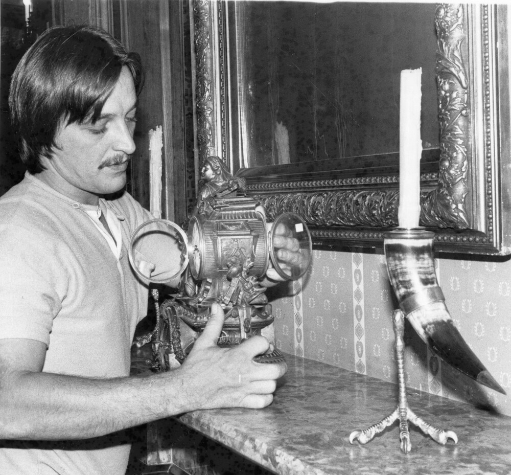 Man holding and cleaning an antique clock on a mantelpiece.