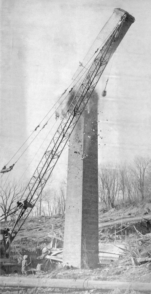 Wrecking ball on a crane strikes a brick chimney tower