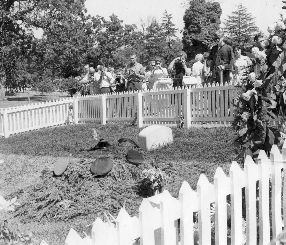 Tourists view a gravesite surrounded by a picket fence.
