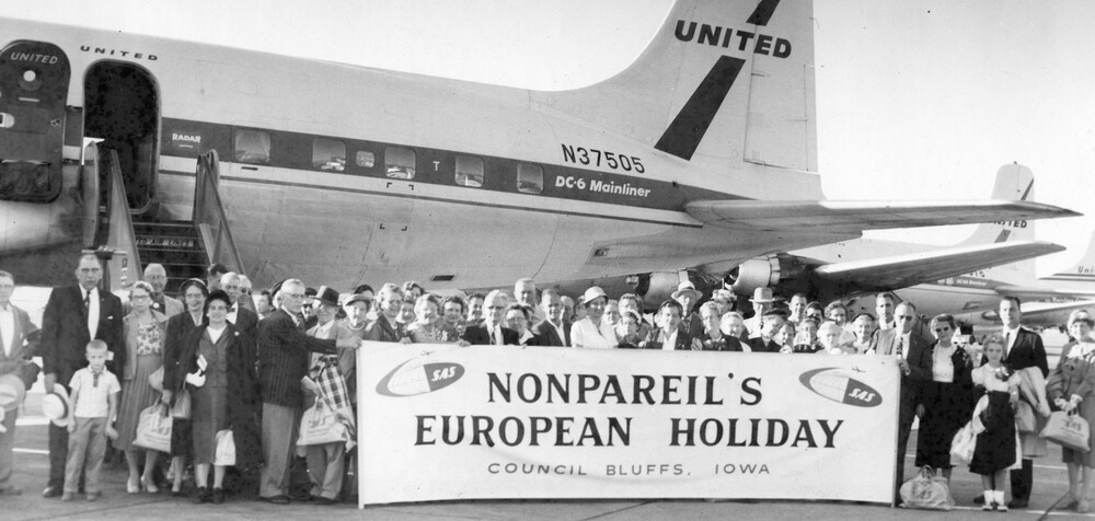 Tour travelers with banner in front of a plane.