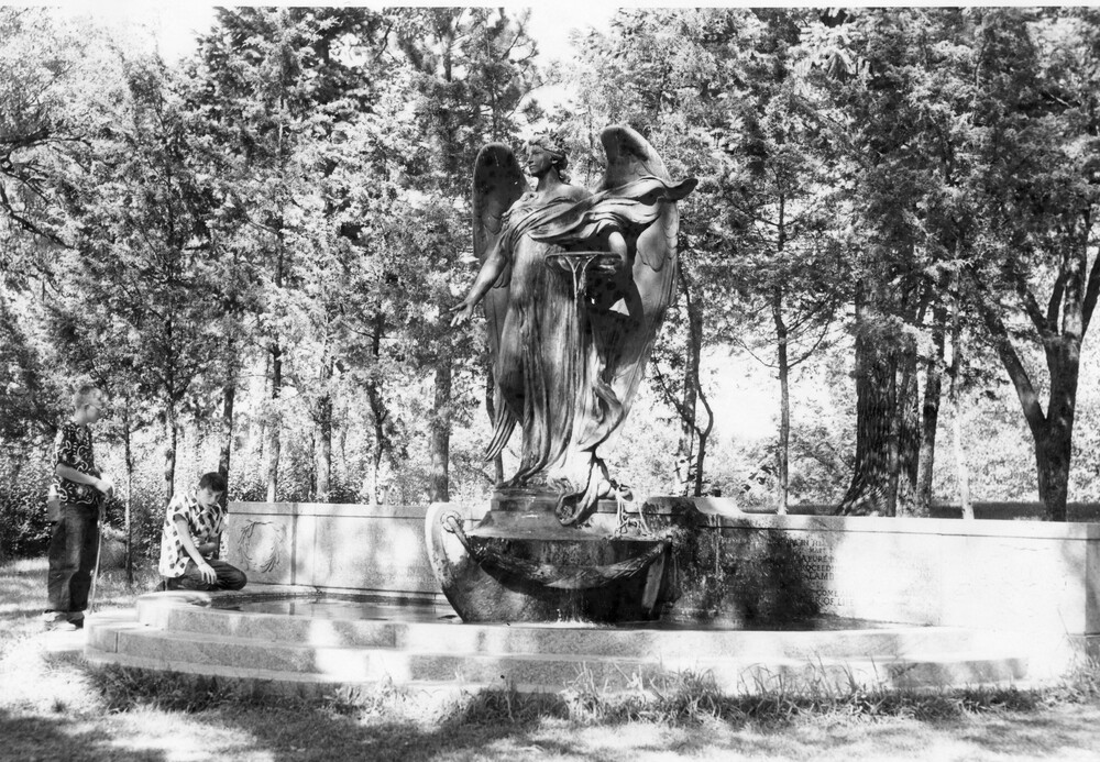 Large statue of angel in the bow of a boat, with short wall and collecting pool