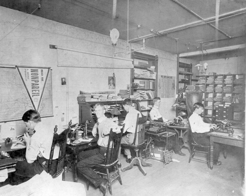 Five young men sitting at desks in a newsroom.