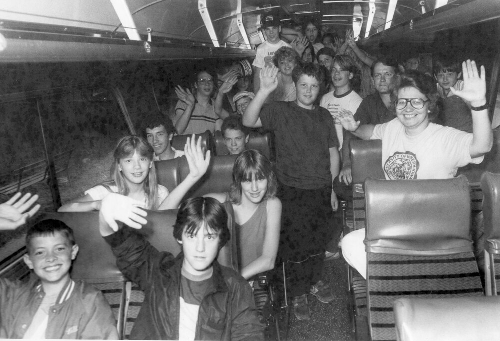 A group of children on a bus waving to the camera.