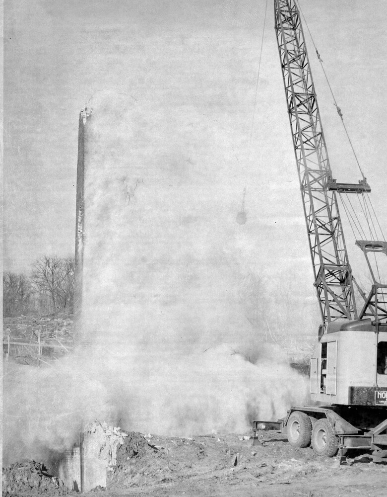 Tall crane in front of cloud of smoke from the demolition of a tower.