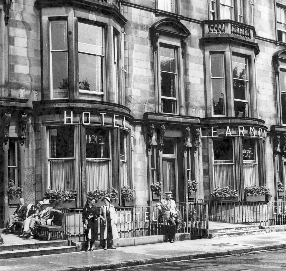 People standing and sitting in front of a hotel.