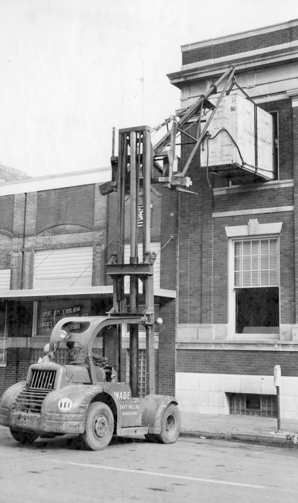 A large piece of equipment atop a hoist in front of a building.
