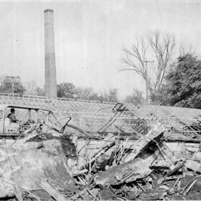 Bulldozer and wreckage from demolition in front of a greenhouse and brick chimney tower