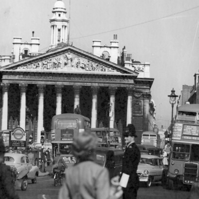 Pedestrians and cars crowd a street in front of a large building.
