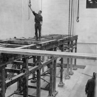 A man stands atop a steel grid structure as another man looks on.