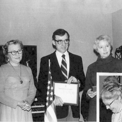 Two women with a man holding an award; a woman inset at bottom right.