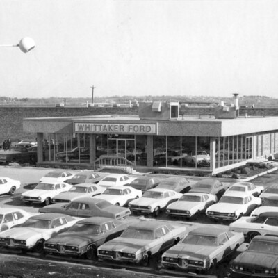 Photo of car lot with building and rows of cars; Ford sign