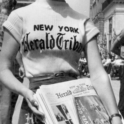 A woman holding a bundle of newspapers.