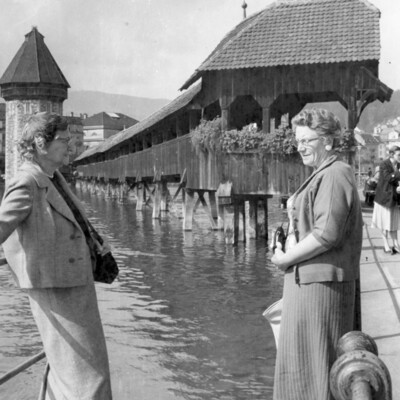 Two women near a covered bridge over water.