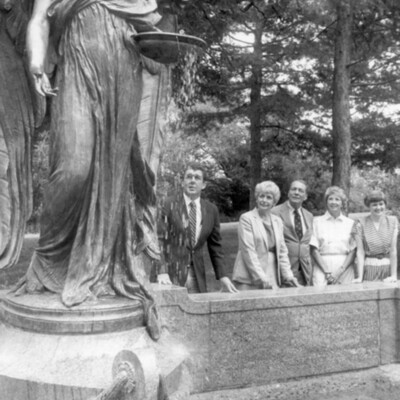 Five people stand behind low wall next to large statue/fountain of an anel