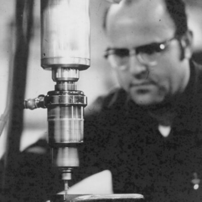 Man sitting behind a drill press.