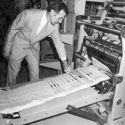 A man looking at newspapers coming off the printing press.