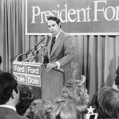 Man in suit at podium, in front of a crowd of people