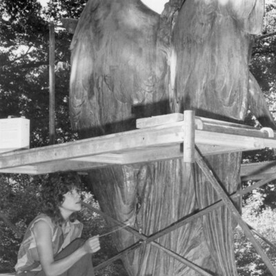 woman sitting under scaffold erected behind a large statue of an angel