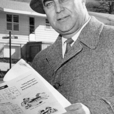 man in overcoat in hat holds several pages of paper