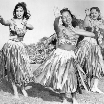 Three dancing women in grass skirts and leis.