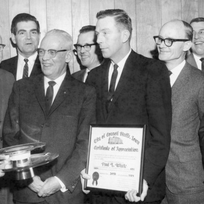 Man holding certificate appreciation, surrounded by eight other men