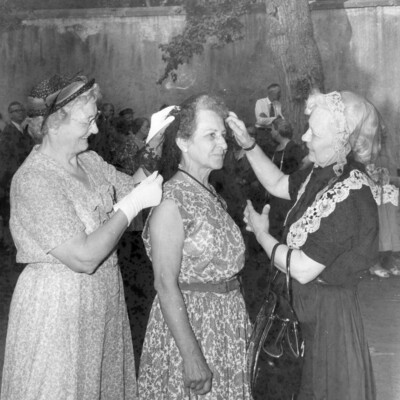 Two women adjusting the chapel veil of another woman. 
