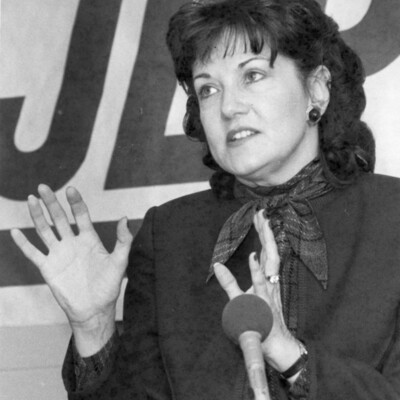 Woman stands behind microphone, gesturing with hands