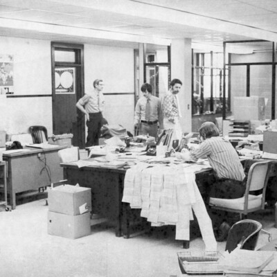 Four men looking at messy desks.
