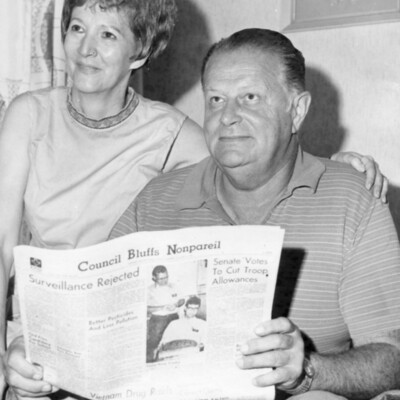 Man holding newspaper, woman beside him with arm around his shoulder