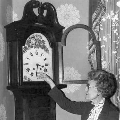 Woman setting the hands of an antique grandfather clock.