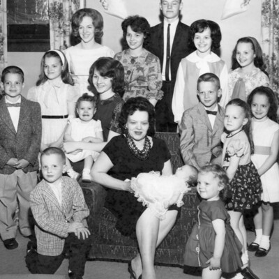 Woman seated, holding a baby, and surround by 14 other children