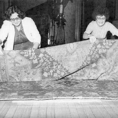 Two women rolling up a large, Persian-style rug.