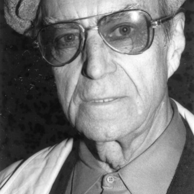Head shot of older man wearing glasses and a cloth cap