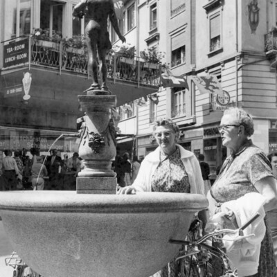 Two women at a fountain on a street.