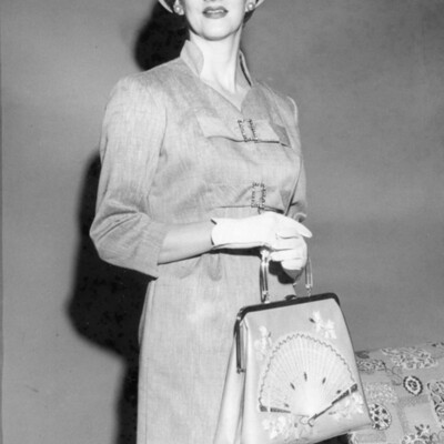 Woman models dress and jacket, cloche hat, and purse
