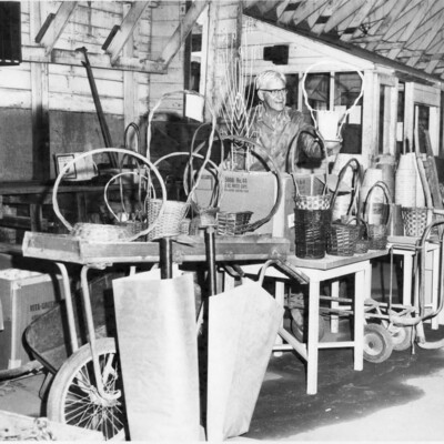 Older man standing by a variety of items, including baskets and dolleys/trolleys.