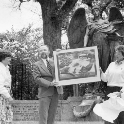 man presenting framed print in front of large outdoor state of an angel