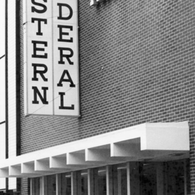 front of brick building with tall windows and architectural overhang