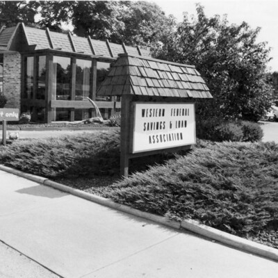 brick and glass building, sign with shingled top, and landscaping