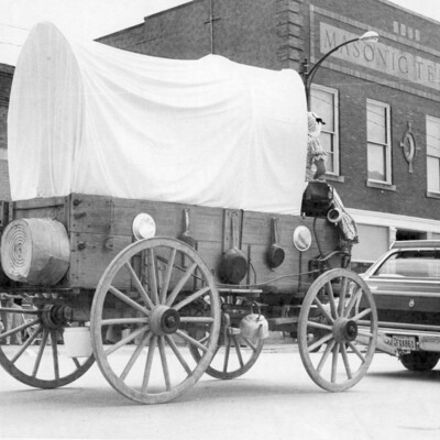 A covered wagon being pulled by a car.