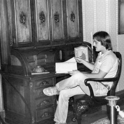 Man sits at rolltop desk, reading a book.