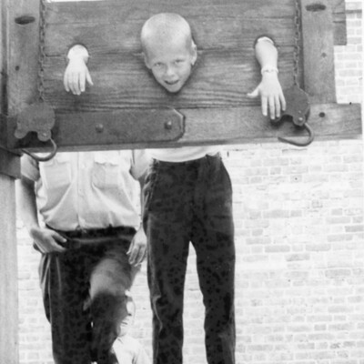 A smiling young man in a stock at a tourist attraction.
