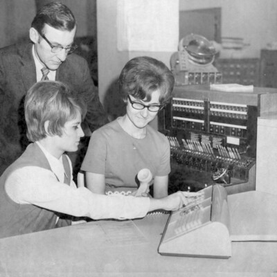 A man and two women viewing a telephone. 