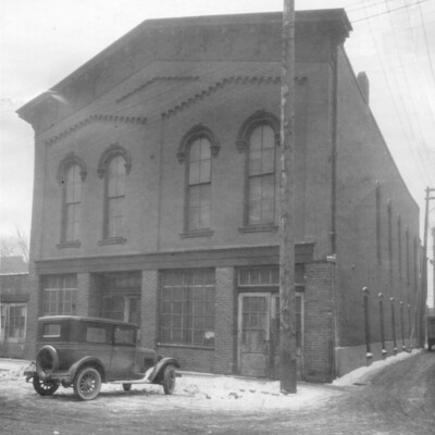 Exterior, front, of two-story brick building with Model T car parked in front.<br />

