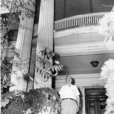 Photo of a man in shirtsleeves standing by columns of the mansion's veranda.