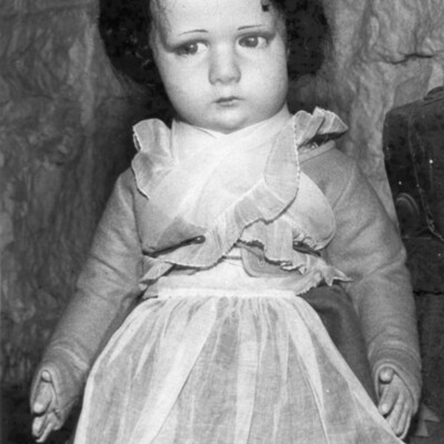 Antique girl doll with dark hair, wearing an apron.