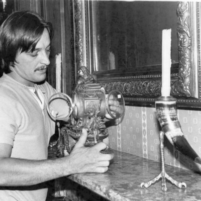 Man holding and cleaning an antique clock on a mantelpiece.