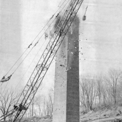 Wrecking ball on a crane strikes a brick chimney tower