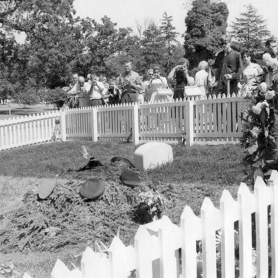 Tourists view a gravesite surrounded by a picket fence.