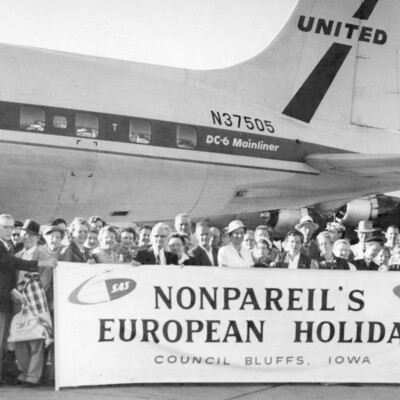 Tour travelers with banner in front of a plane.